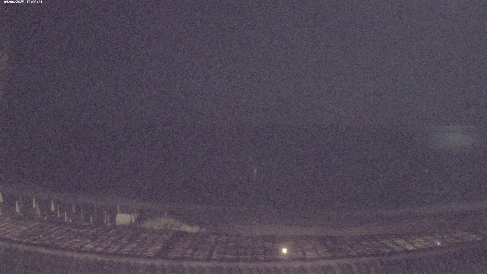 A low-light nighttime image shows a dark field with rows of what appear to be plants or crops, and some light-colored markers or stakes in the distance.