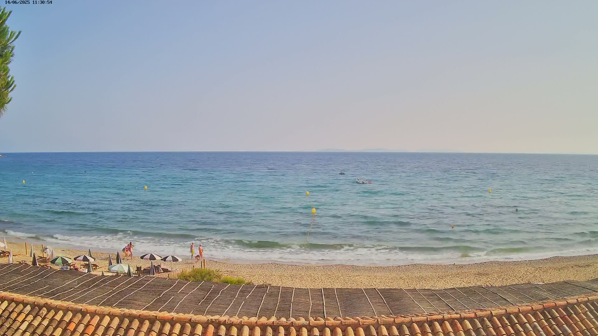 A sandy beach with a few people and umbrellas is visible, overlooking a calm, light-blue ocean under a clear sky.