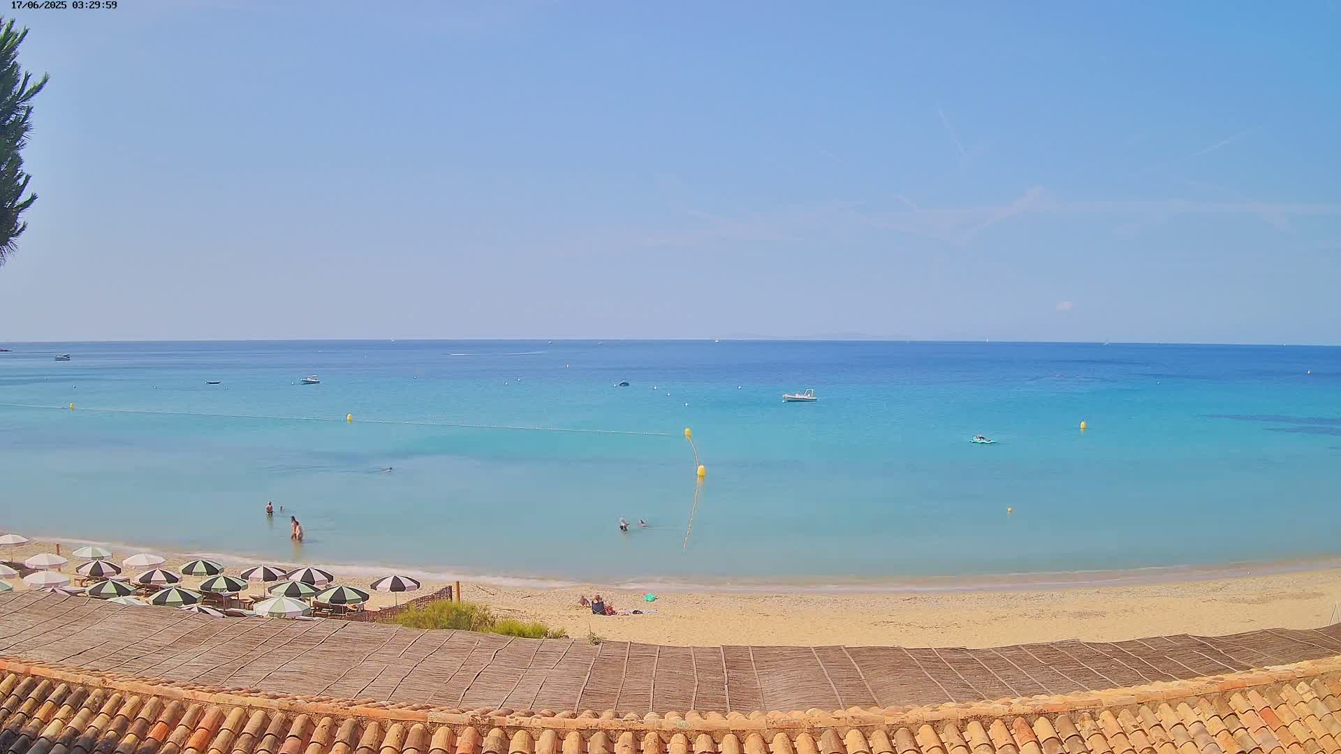 A sandy beach with turquoise water and several people swimming, under a clear blue sky.