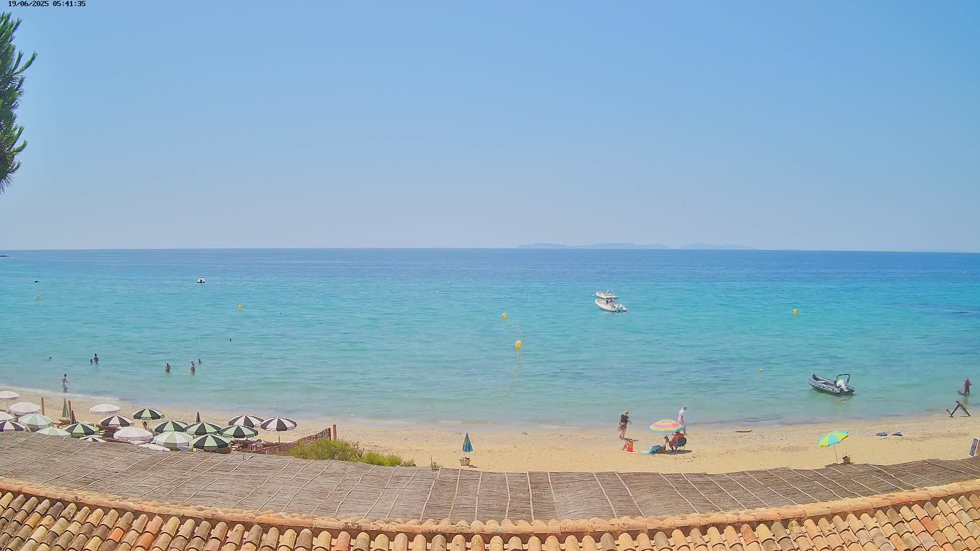 A sandy beach with turquoise water, several people, and umbrellas is visible under a clear blue sky.