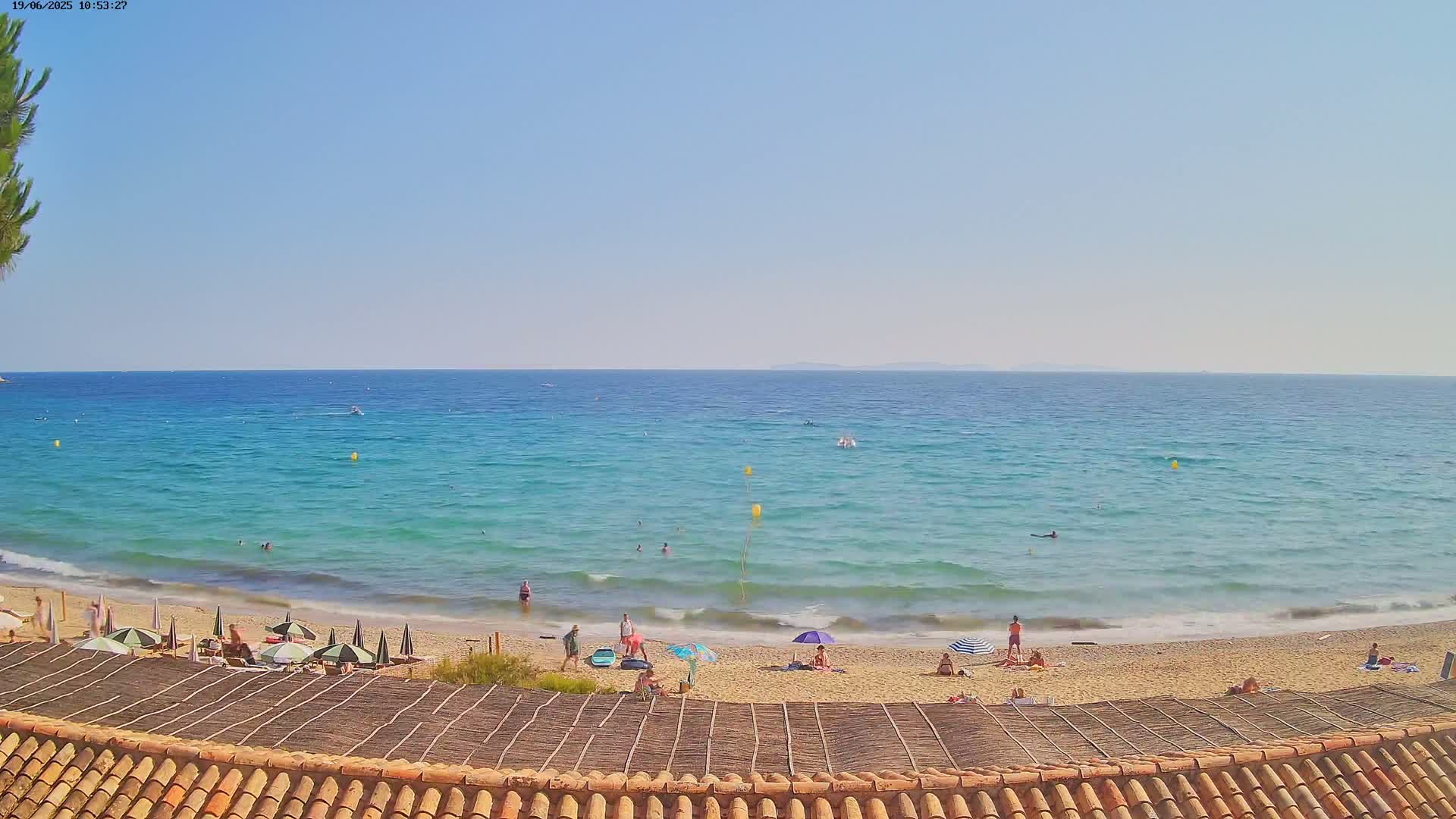 A sandy beach with turquoise water and scattered beachgoers under umbrellas on a sunny day.