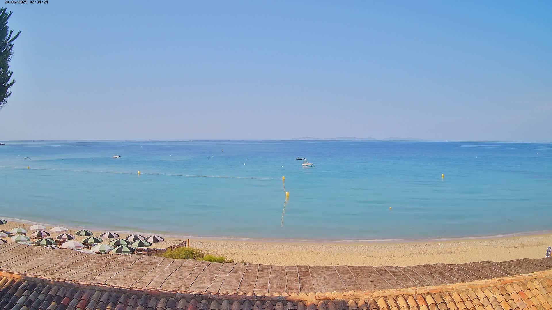 A sandy beach with turquoise water and several closed umbrellas sits under a clear blue sky.
