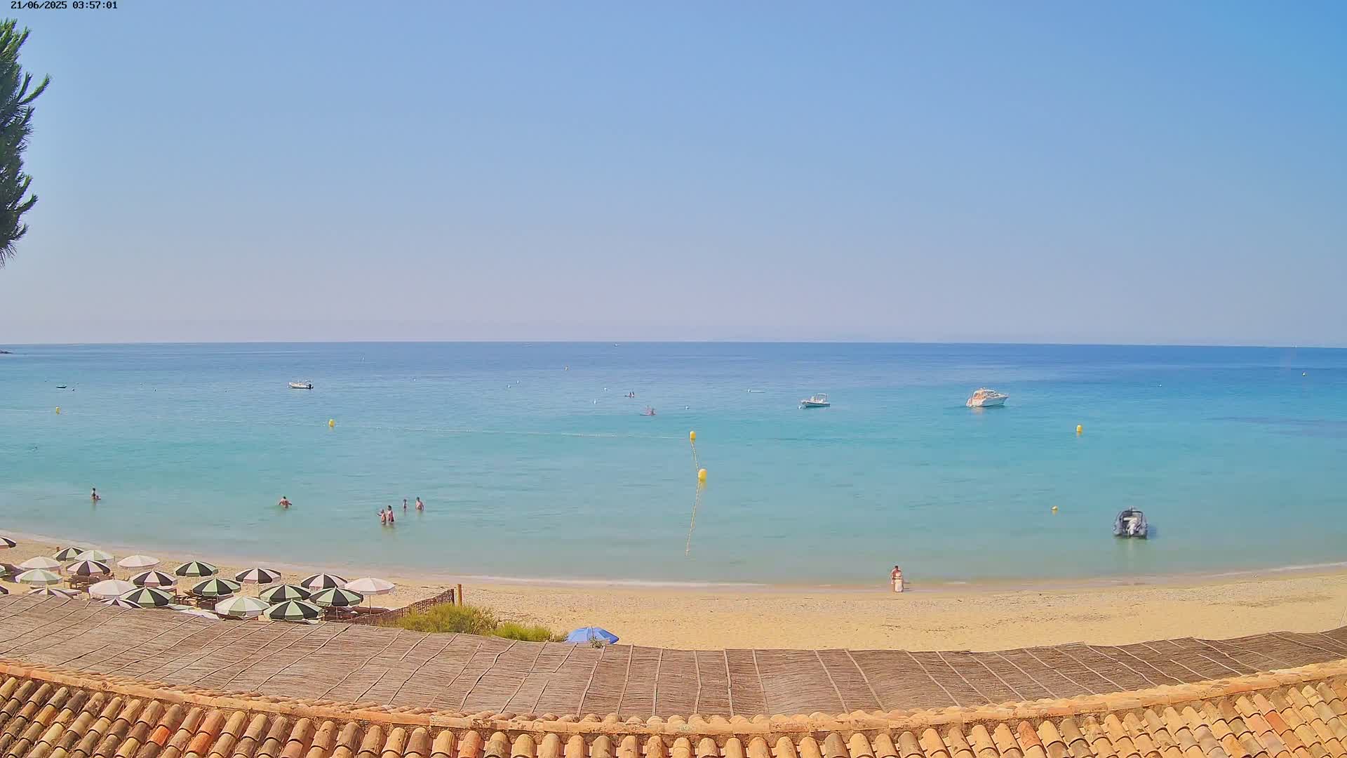 A sandy beach with turquoise water and several people swimming and sunbathing under umbrellas on a clear, sunny day.