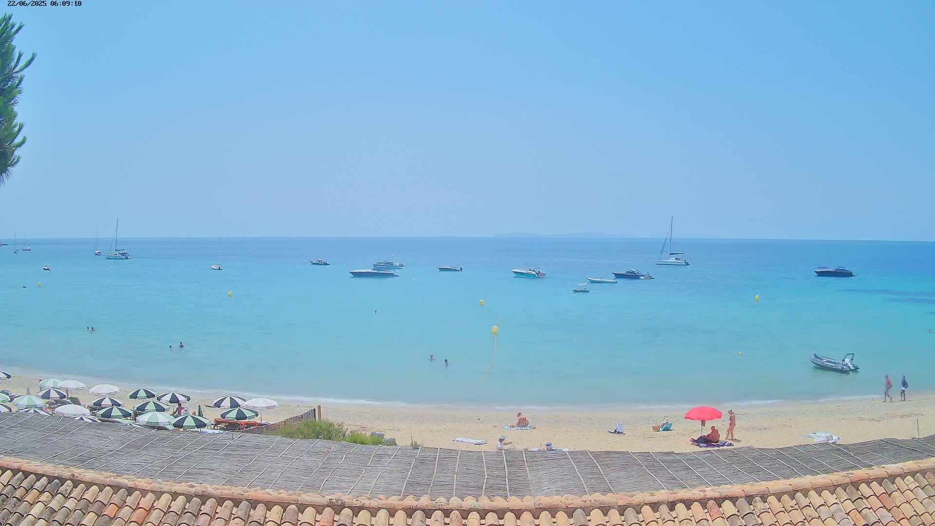 A sandy beach with turquoise water and several boats anchored offshore on a sunny day.