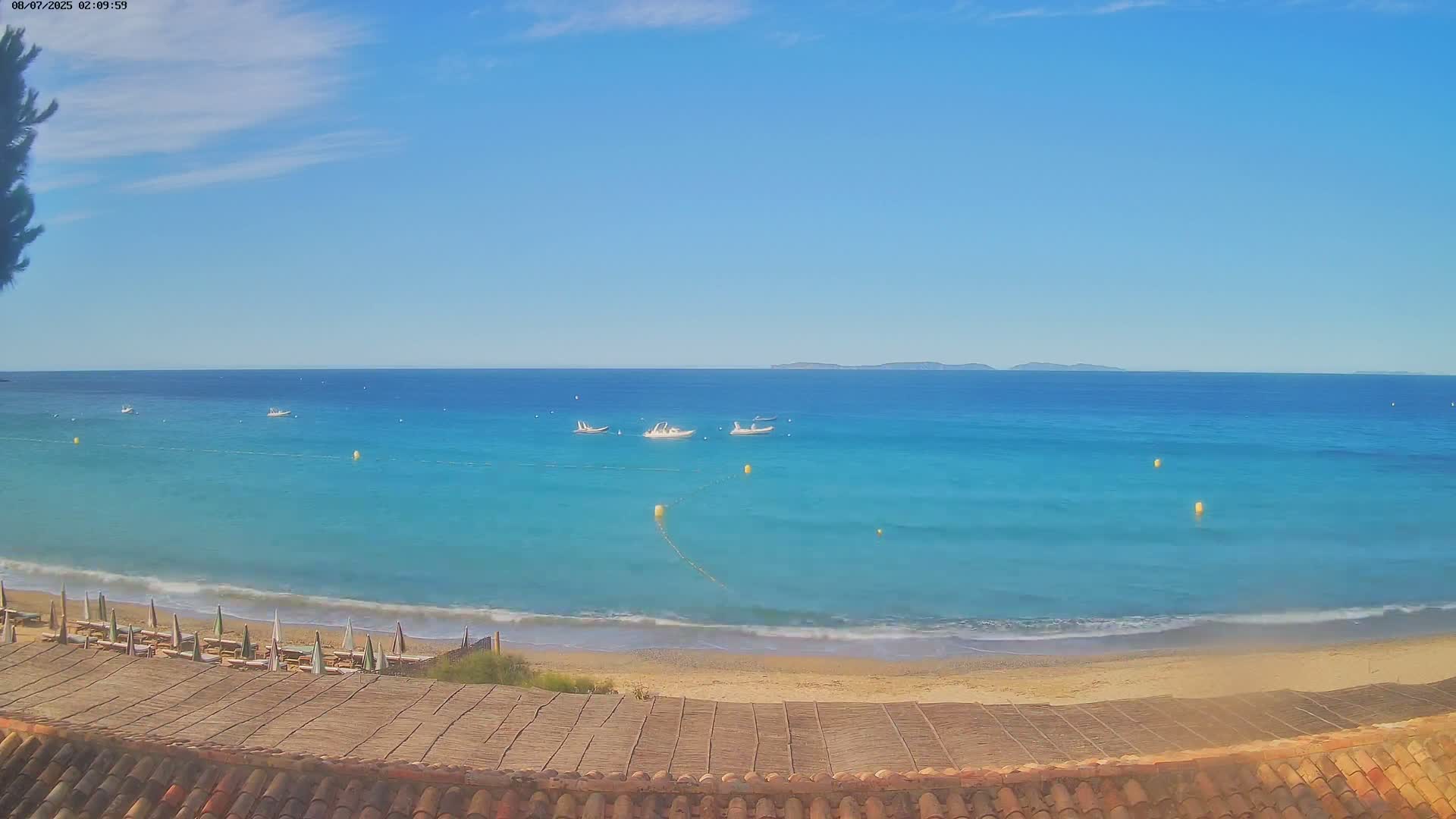 A sandy beach with turquoise water and several small boats offshore under a clear, sunny sky.