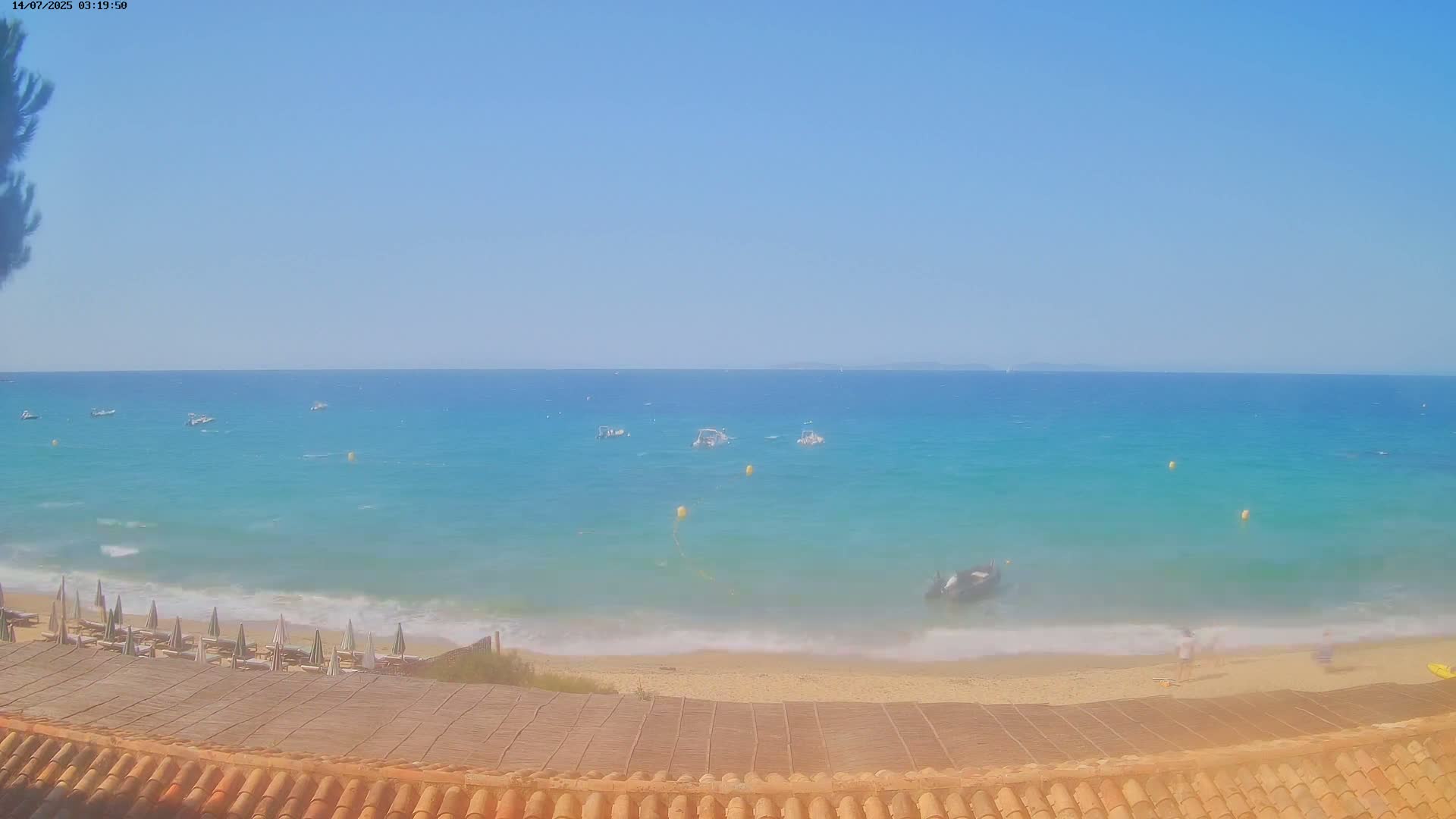 A sandy beach with several small boats offshore on a clear, sunny day with light waves.