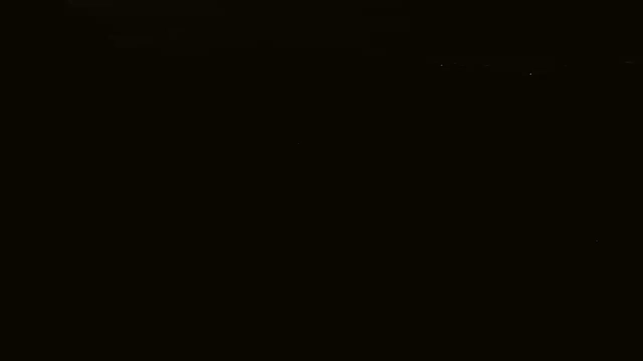 A nighttime, dark scene shows a few distant lights in the far background.