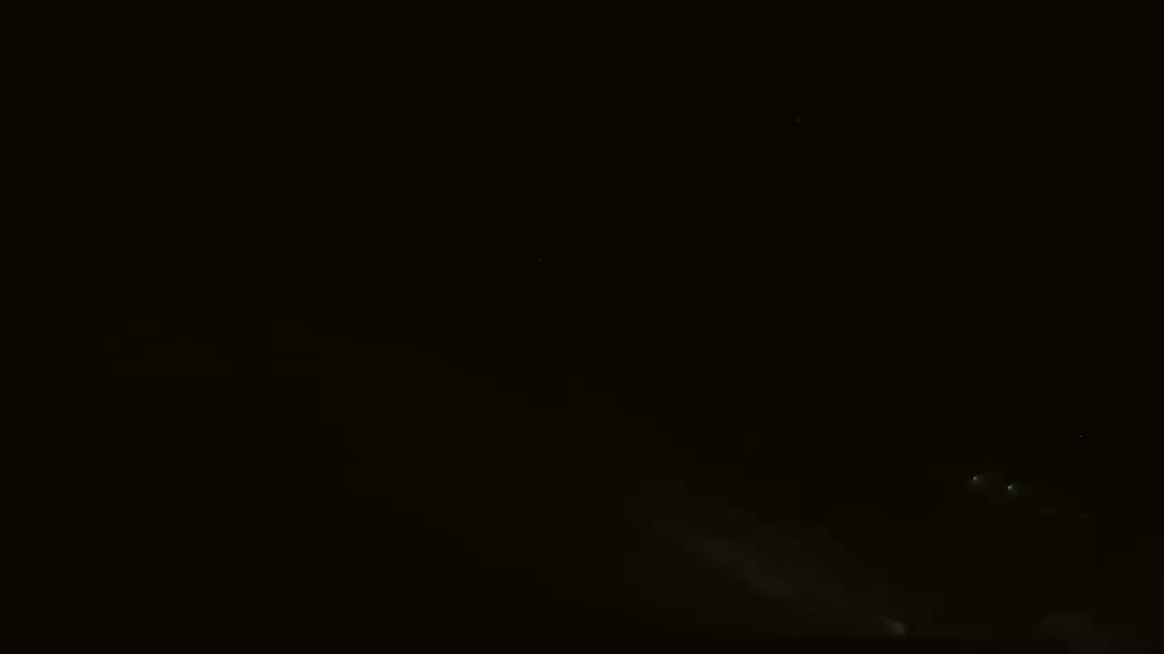 A dark, nighttime scene shows faint lights and what appears to be low-lying fog or mist.