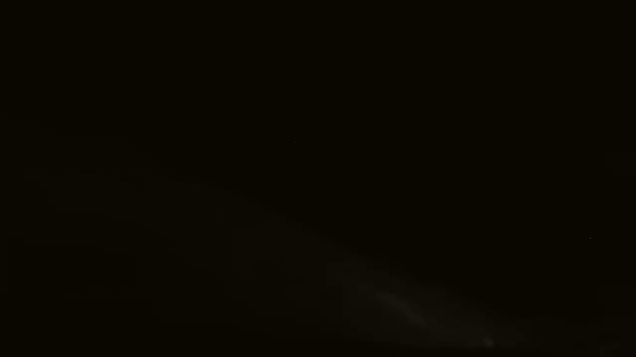 A dark, nighttime scene shows a faint, light-colored plume rising from the bottom.