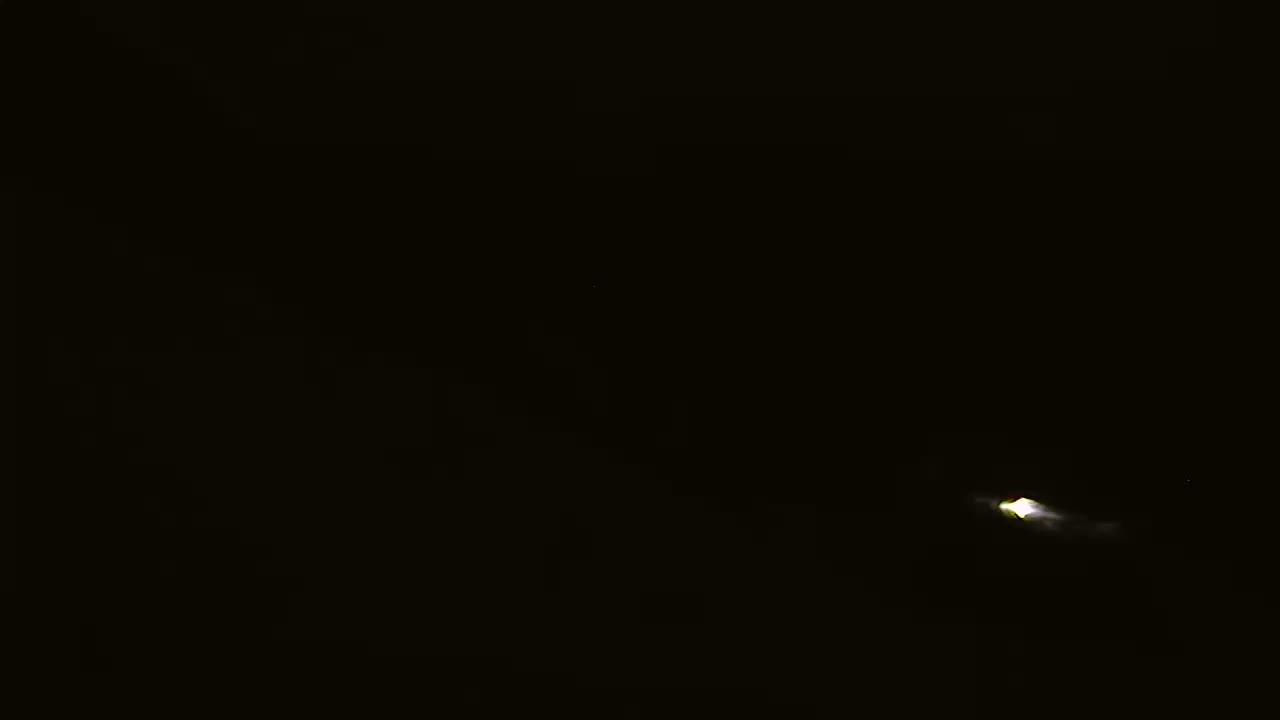 A faint, luminous object is visible in a dark, nighttime sky.