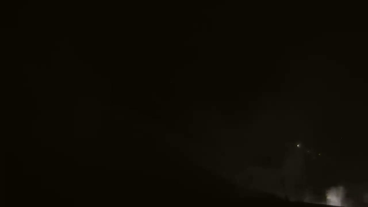 A dark night sky shows faint, distant lights and a low-lying, hazy fog or steam near the bottom.