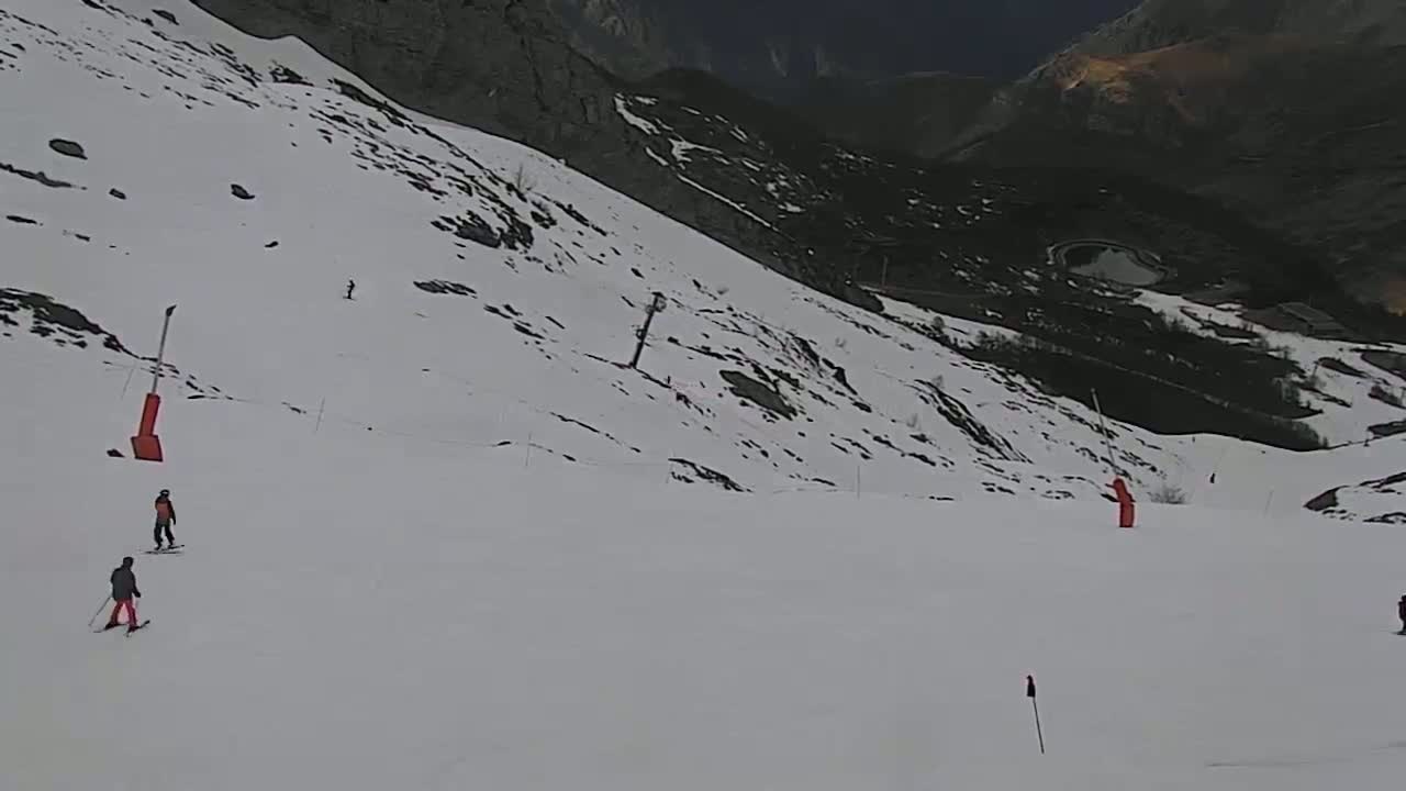 A snowy mountain slope with several skiers and ski lift equipment, under overcast skies.