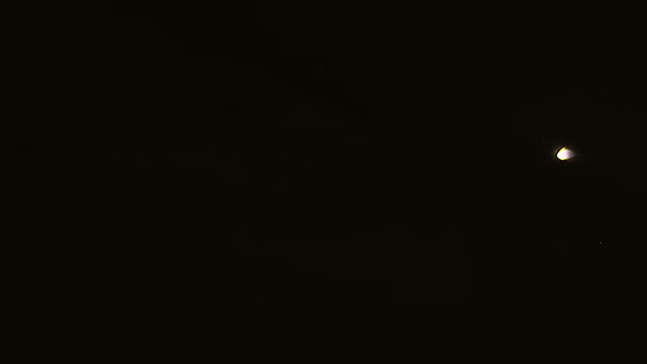 A bright light, possibly the moon or a planet, is visible in a dark night sky with a few faint stars.