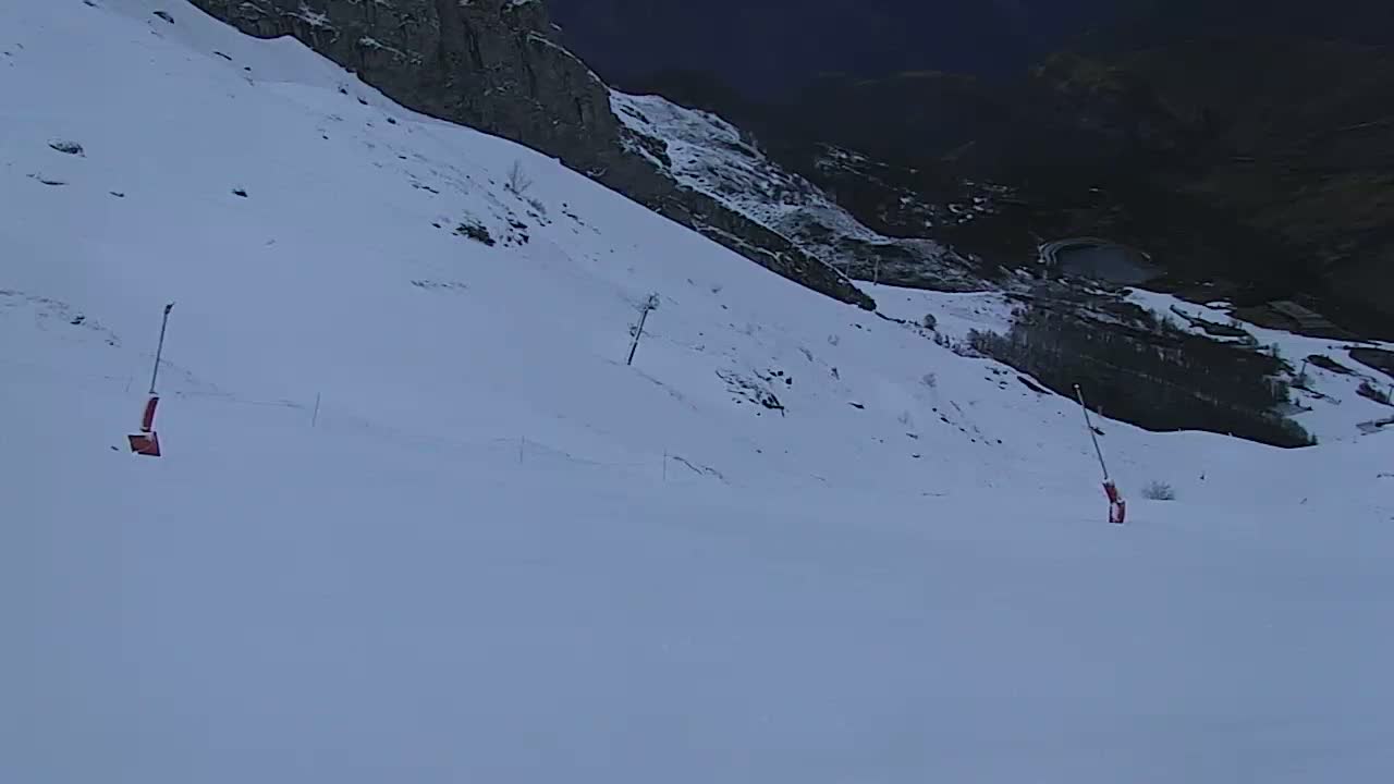 A snow-covered ski slope descends from a rocky mountainside under a dark, twilight sky.