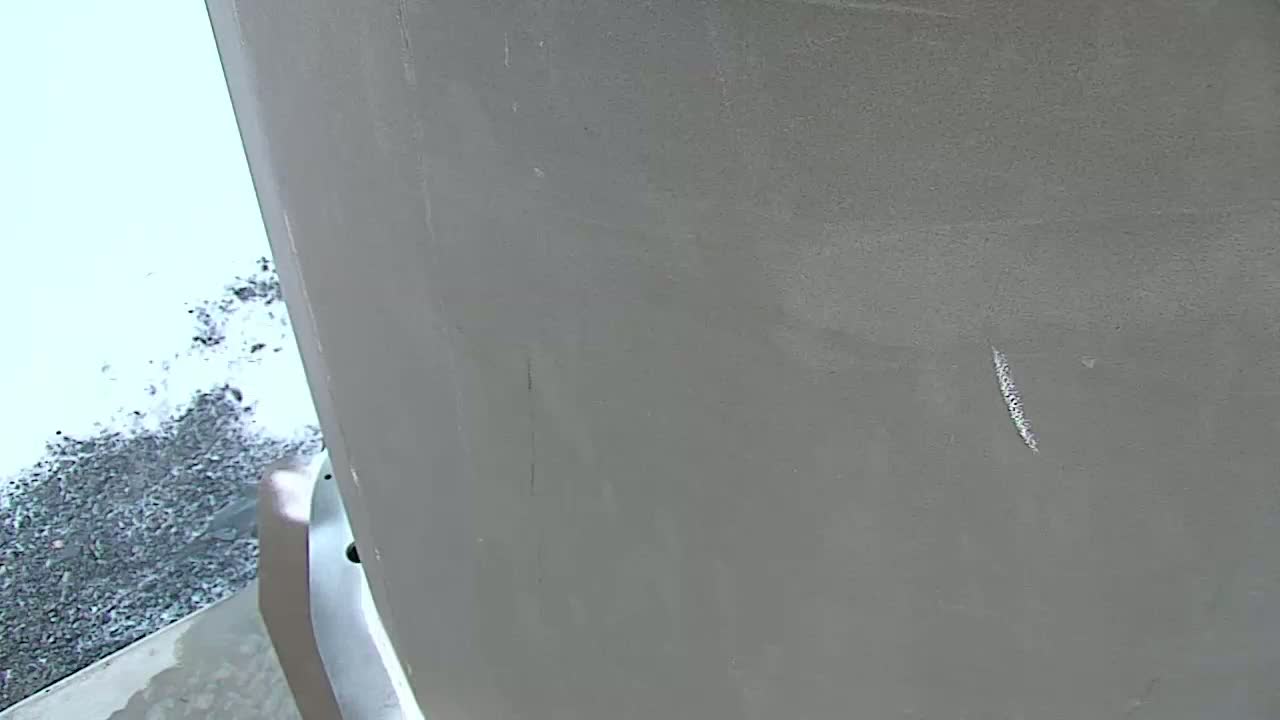 A close-up view shows a large, light gray surface with a few faint scratches and a pile of dark gray debris in the bottom left corner.