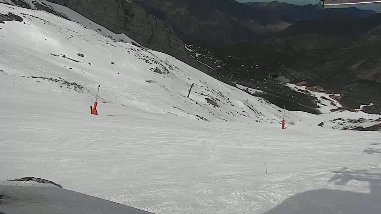 A snowy ski slope descends into a mountainous valley under sunny conditions.