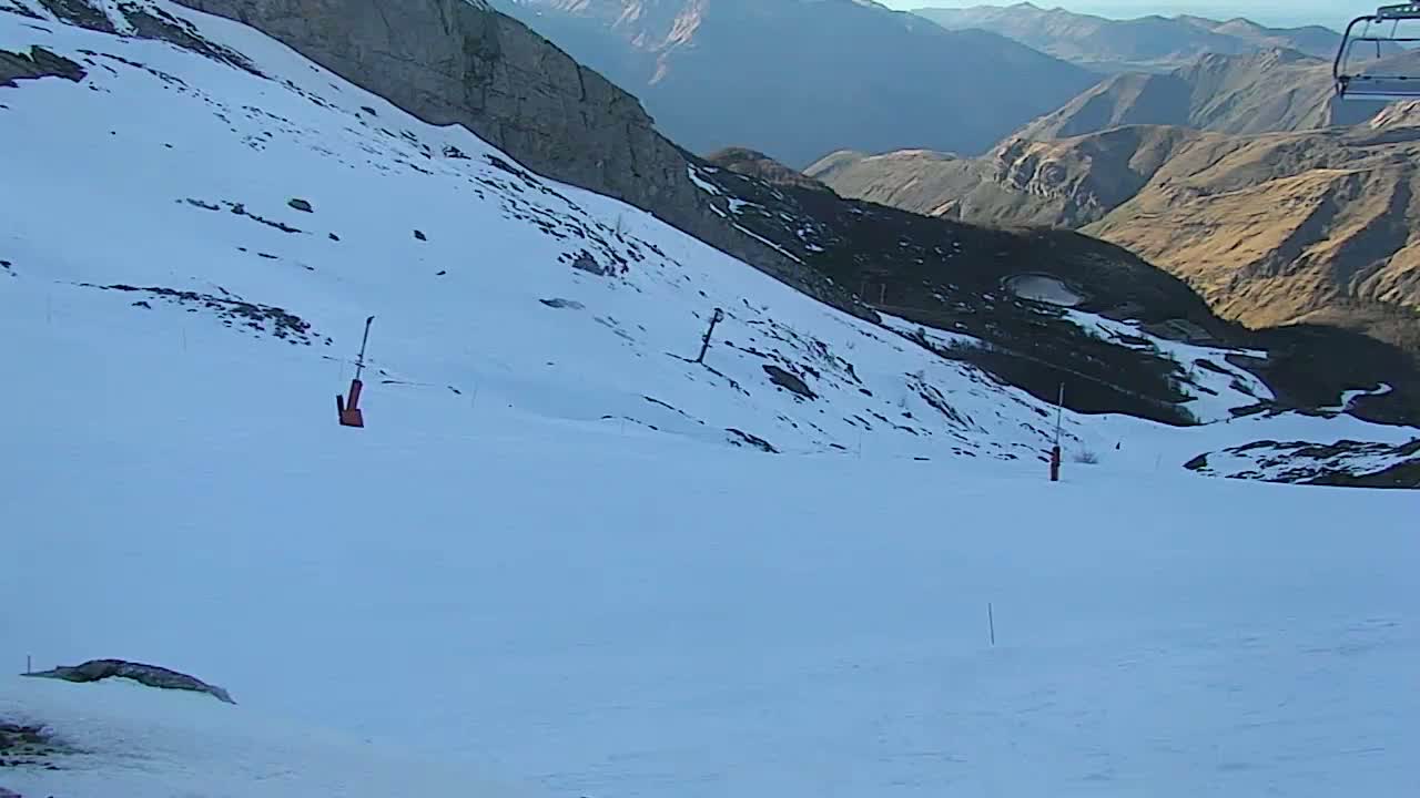 A snow-covered mountain slope with a chairlift in the background under a clear sky.
