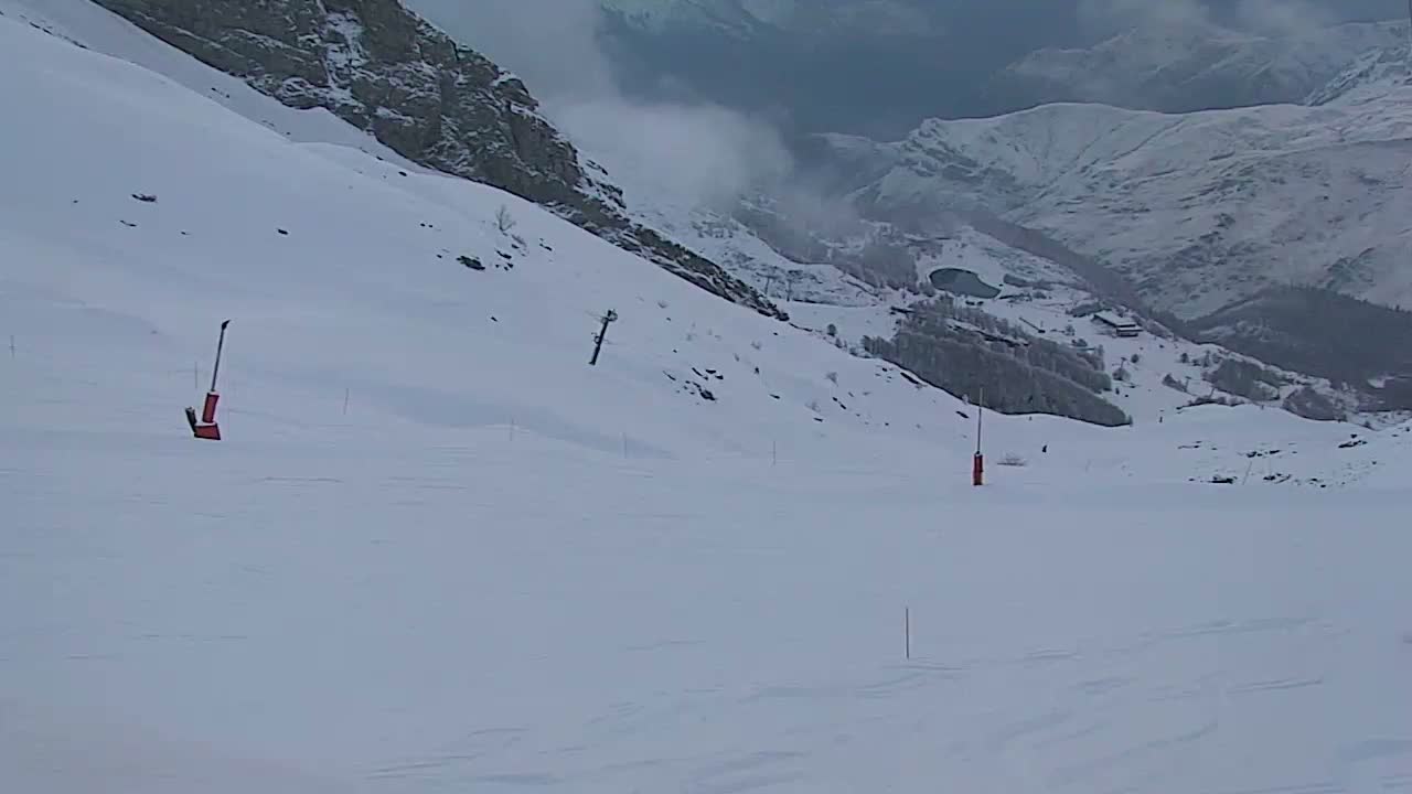 A snowy mountain slope with two red markers and a ski lift in the background, under overcast skies.