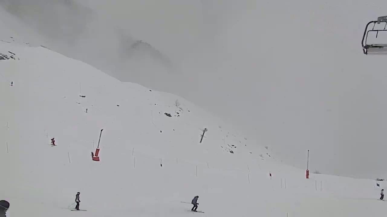 A snowy ski slope with several skiers is visible under foggy conditions, and a chairlift is seen in the upper right corner.