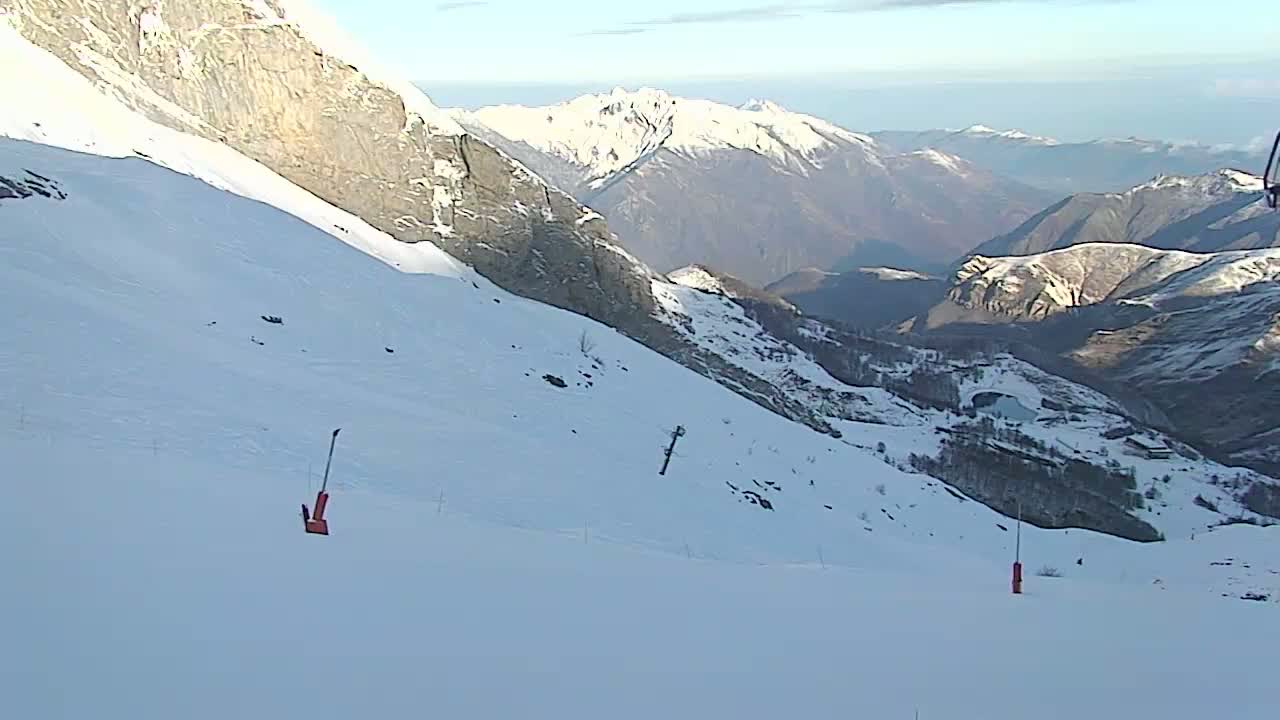 A snowy mountain slope overlooks a valley of snow-covered mountains under a bright, clear sky.