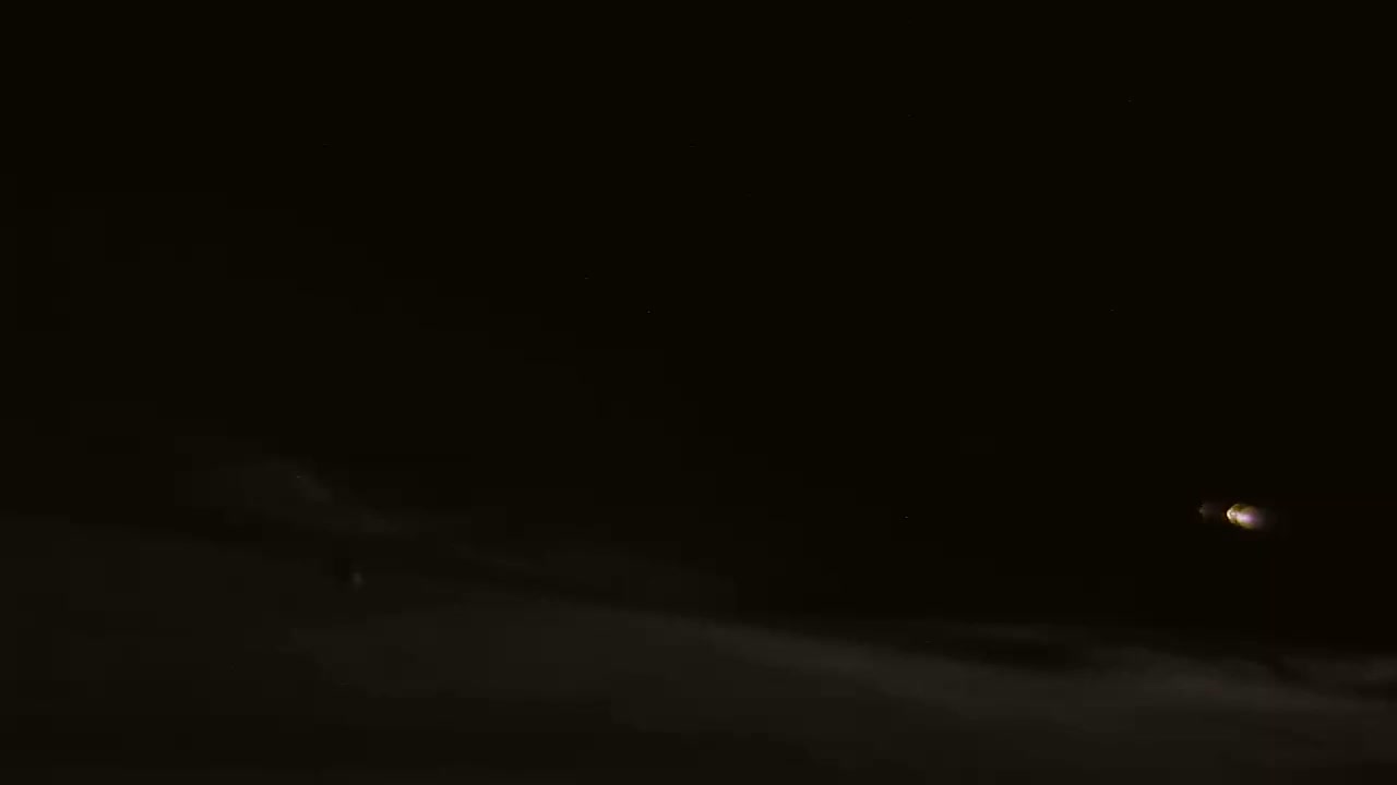 A bright light, possibly a moon or planet, is visible in a dark night sky above a layer of low-lying clouds.