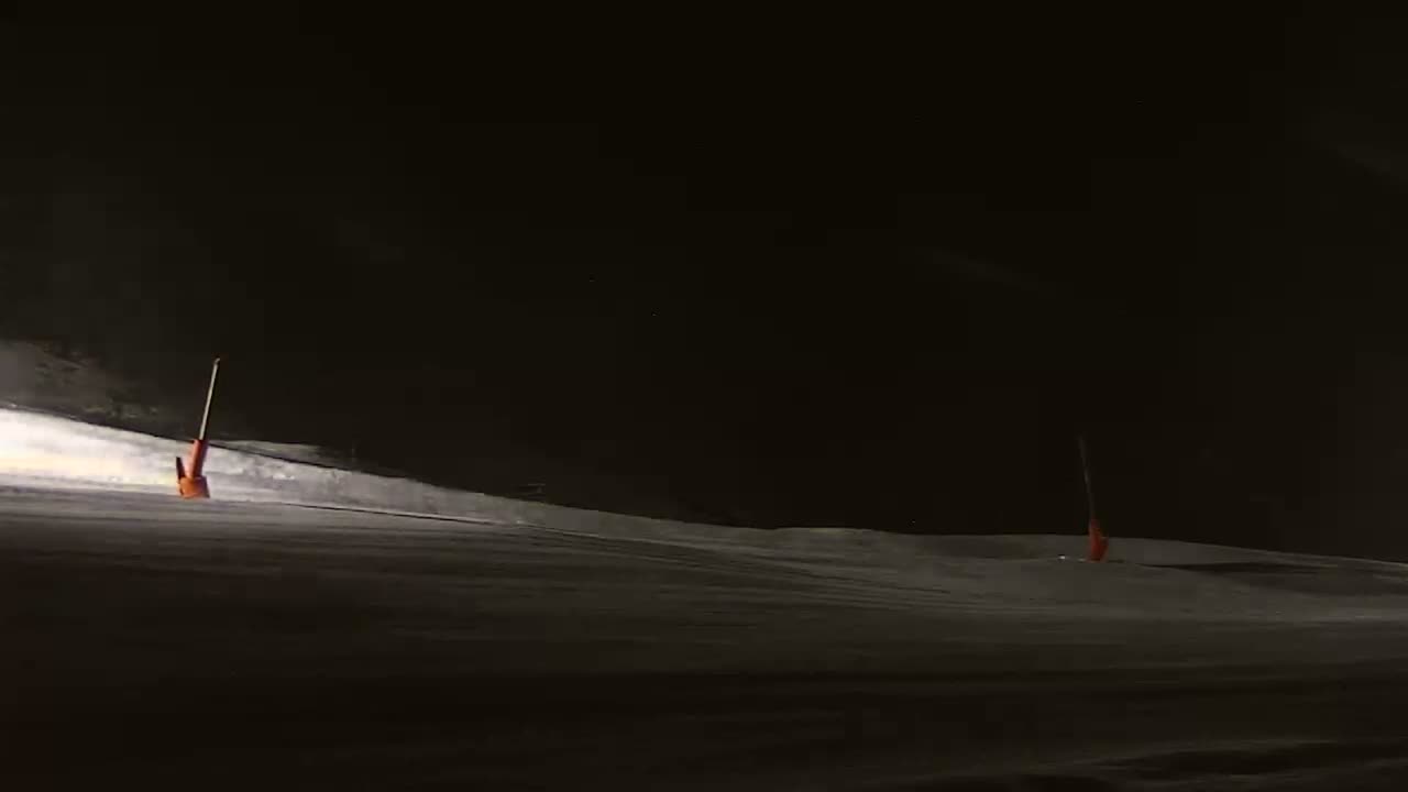 A snow-covered slope at night is illuminated, showing two orange markers.