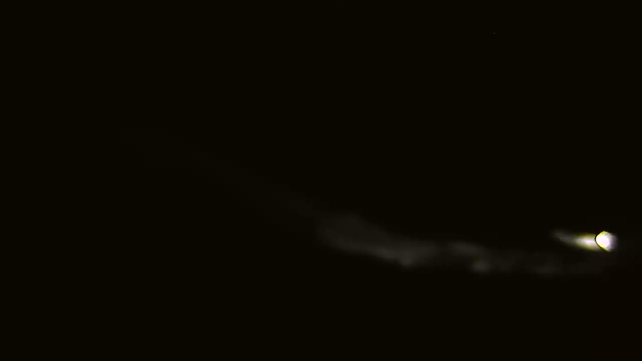A bright light with a faint trail is visible in a dark, cloudy night sky.