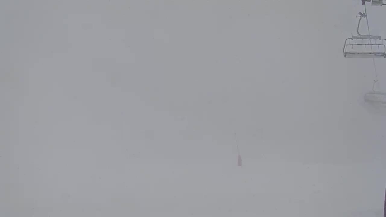A ski lift chair hangs in the heavy snow, obscuring the view.