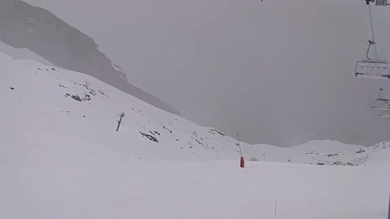 A snow-covered ski slope with a chairlift in the background during an overcast day.