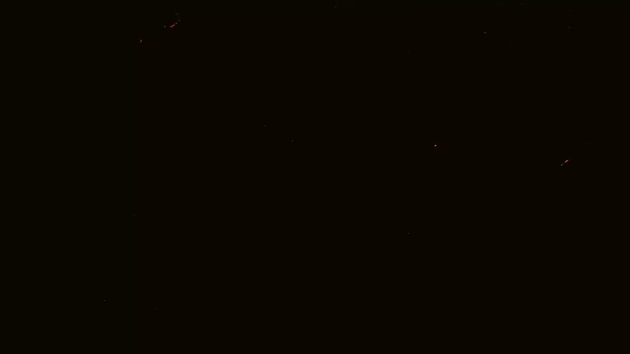 A mostly black image with a few small, faint red and orange specks scattered across it.