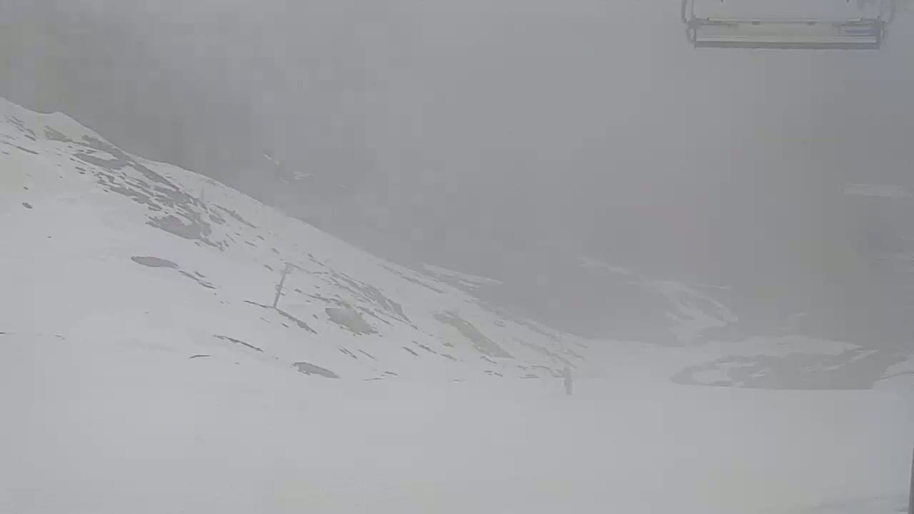 A snow-covered hillside is obscured by heavy fog or blowing snow.