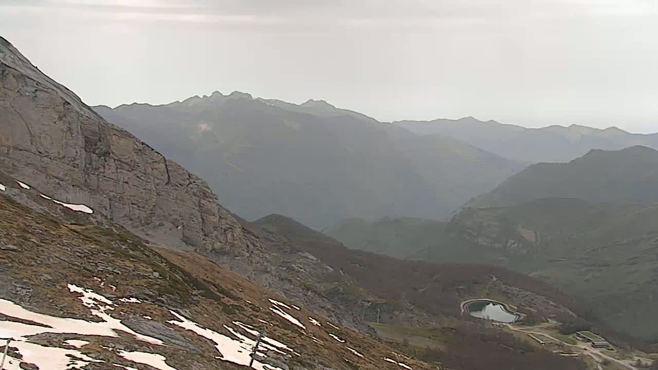 A mountainous landscape with patches of snow, a small reservoir, and hazy weather conditions.