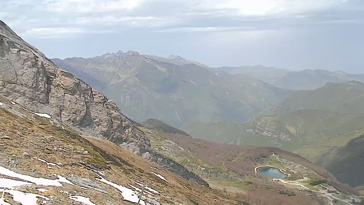 A high-angle view shows a mountainous landscape with patches of snow, a small reservoir, and hazy weather conditions.