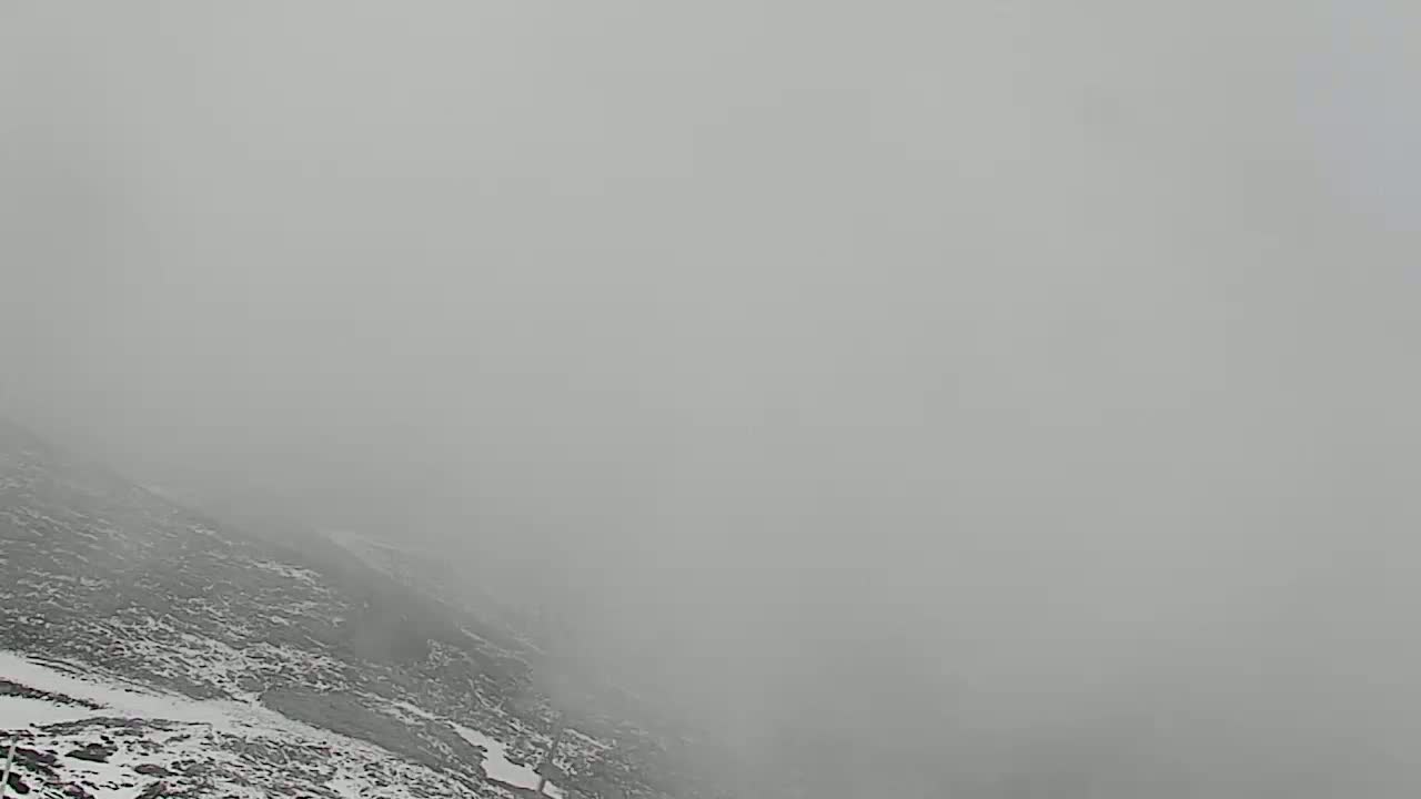 A snow-covered, rocky hillside is obscured by thick fog.