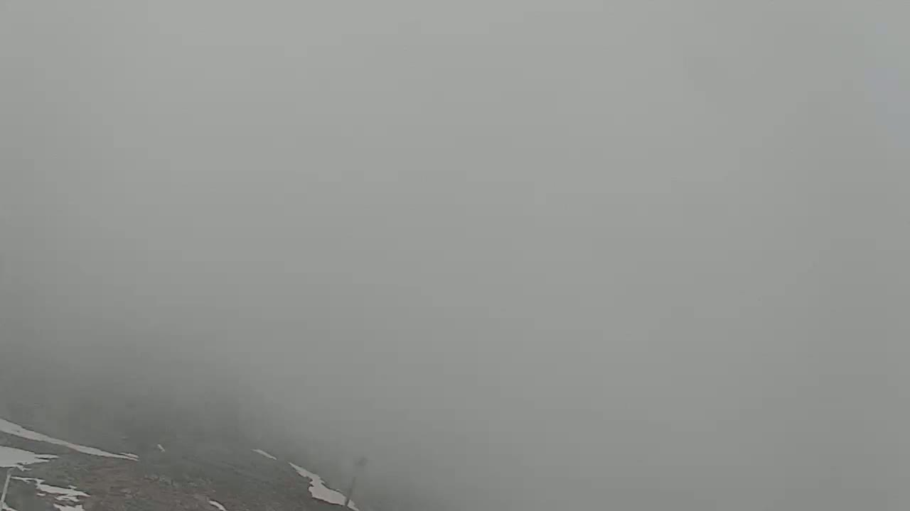 A foggy, mountainous landscape with patches of snow is visible in the lower portion of the frame.