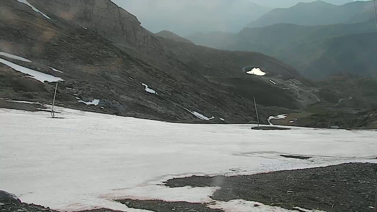 A snowy mountain pass is visible, with dark, rocky mountains in the background under an overcast sky.