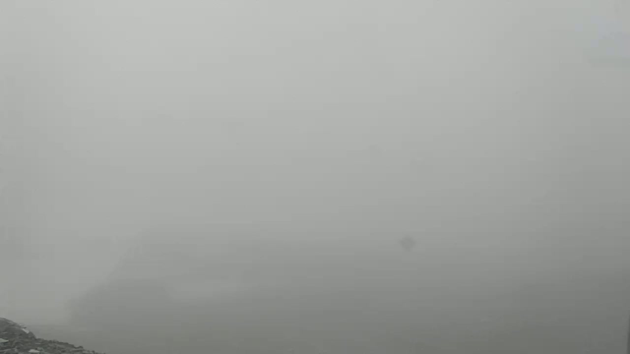 A rocky, lower left corner is barely visible beneath a dense fog that obscures the view.