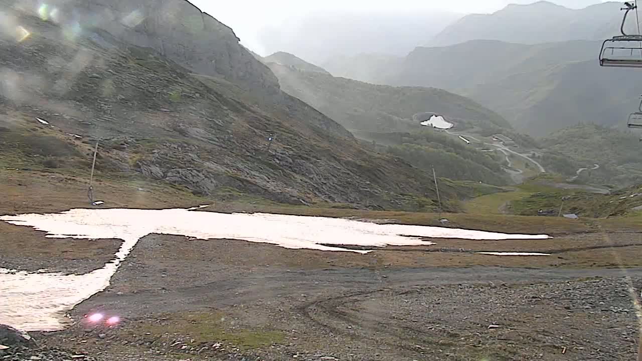 A patch of melting snow sits on a rocky, mountainous landscape under an overcast sky.