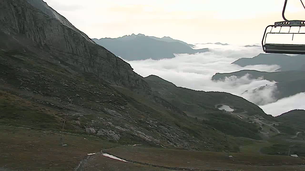 A mountainside with a chairlift partially visible overlooks a valley shrouded in low-lying clouds.