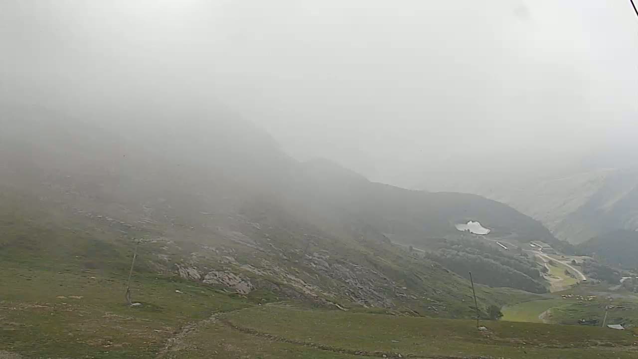 A foggy, mountainous landscape with a valley containing some structures and vegetation visible in the distance.