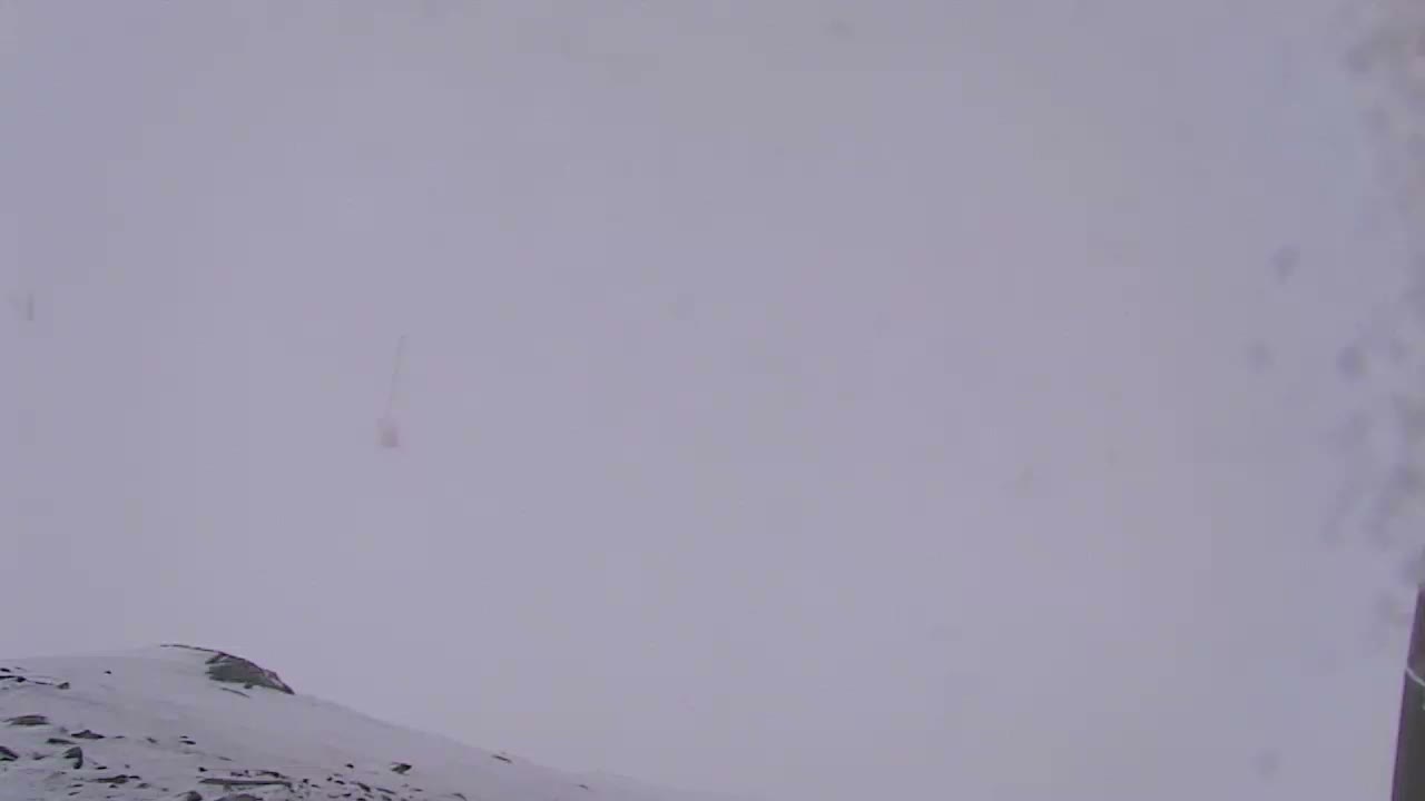 The image displays a snow-covered mountain landscape under overcast skies with very poor visibility due to heavy snowfall.