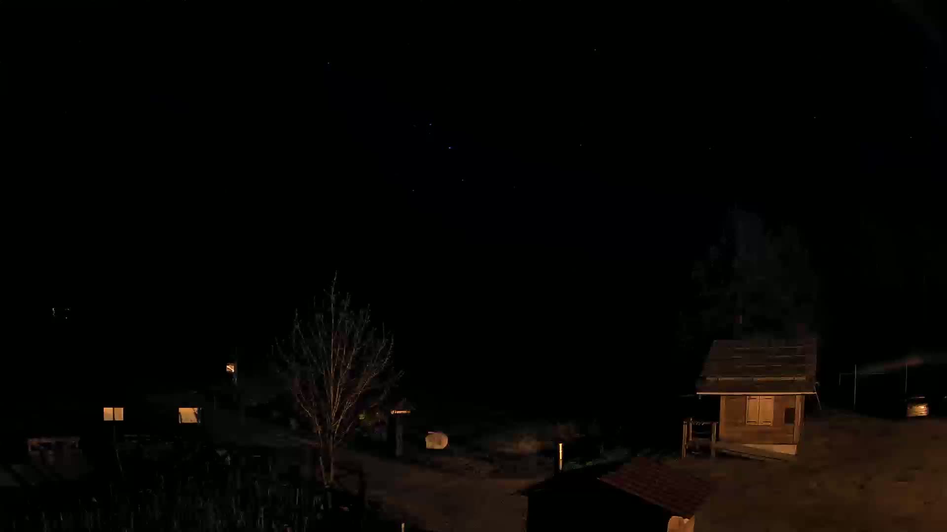 A nighttime view shows several small buildings and a bare tree under a clear, starlit sky.