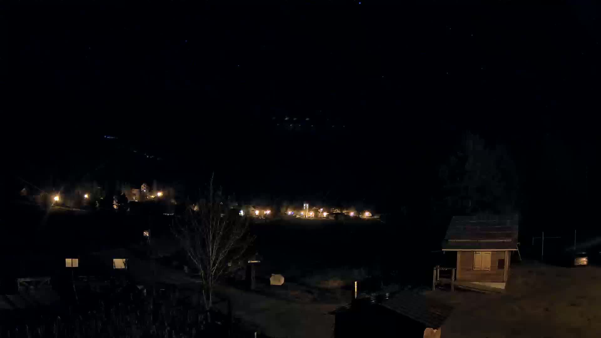 A nighttime view of a small village nestled in a dark landscape under a clear, starry sky.