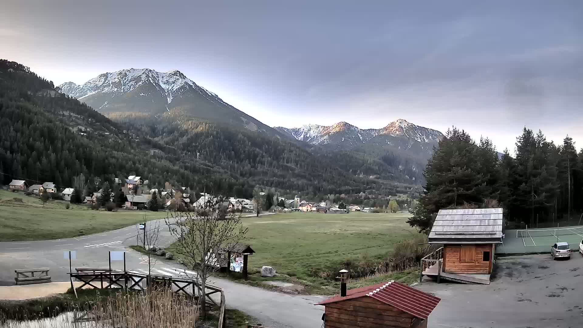 A small village nestled in a valley between snow-capped mountains under an overcast sky.