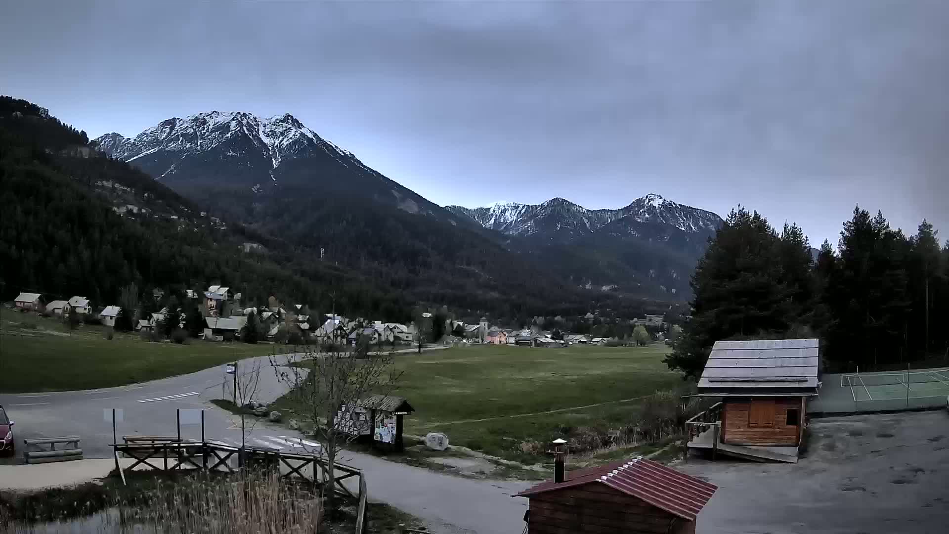 A small village nestled in a valley between snow-capped mountains under an overcast sky.