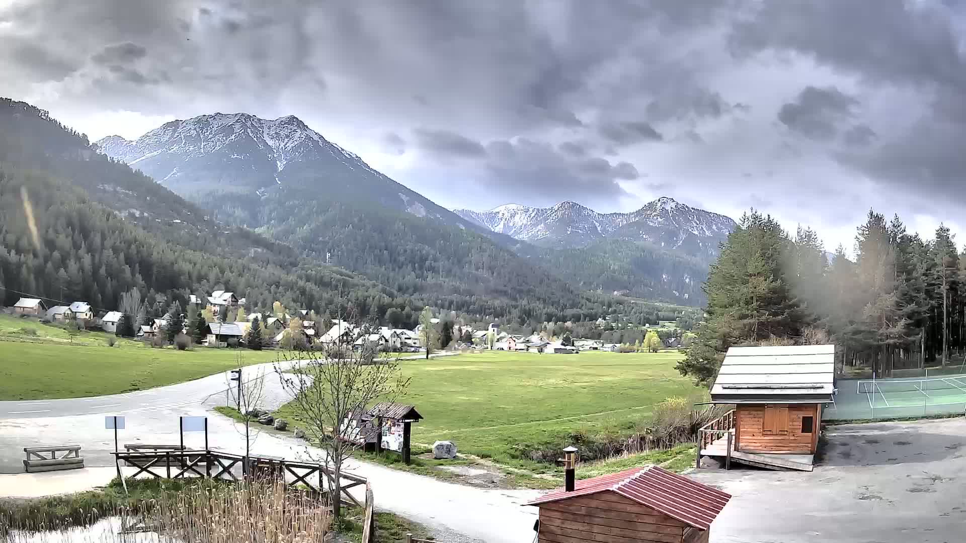 A small village nestled in a valley between snow-capped mountains under a cloudy sky.