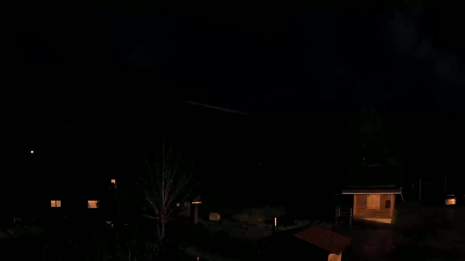 At night, several dimly lit buildings are visible under a dark, cloudy sky.