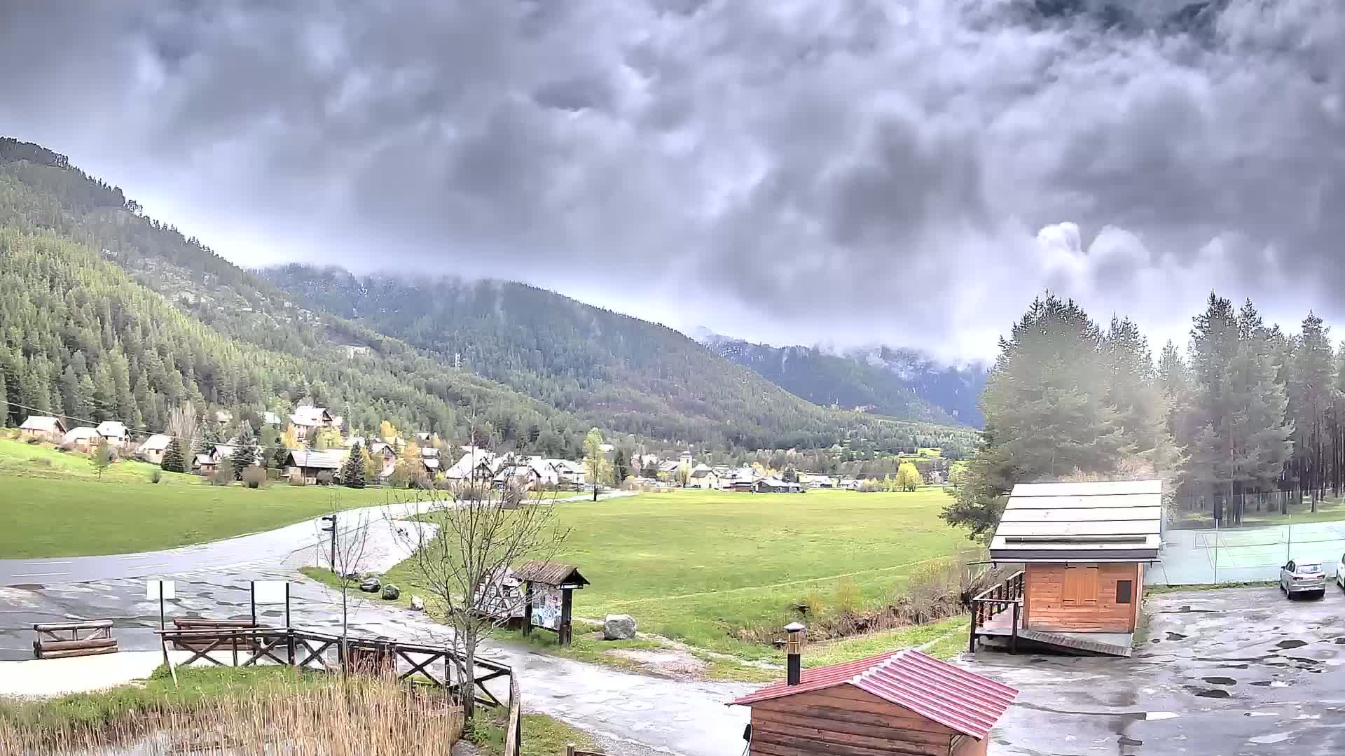 A small village nestled in a valley between forested mountains under a cloudy, overcast sky.
