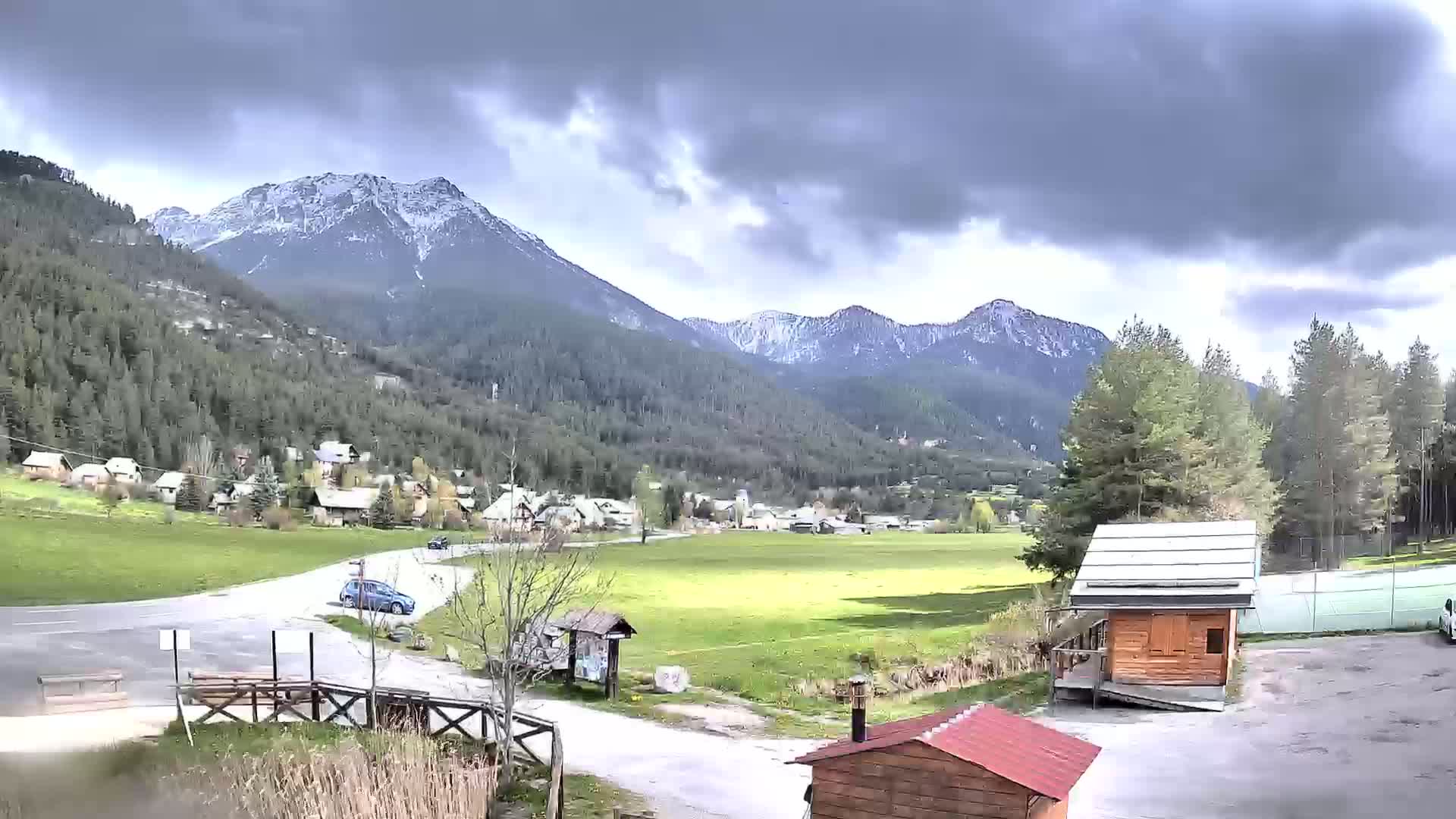 A small village nestled in a valley between snow-capped mountains under a cloudy sky.