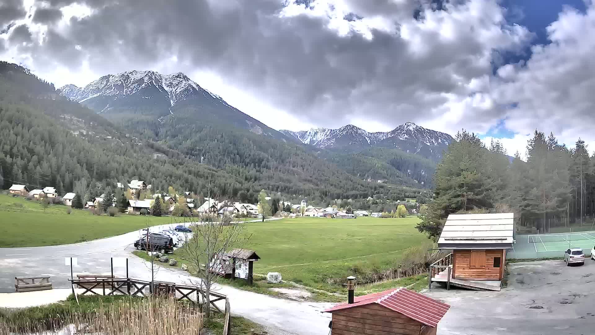 A small village nestled in a valley between snow-capped mountains under a partly cloudy sky.